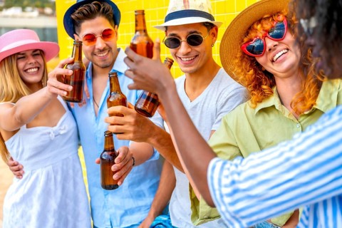 Group of cheerful multiracial young people wearing summer clothes and hats toasting and drinking