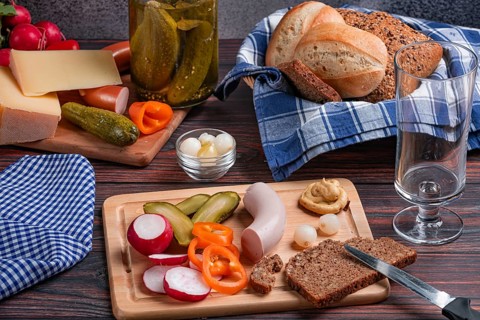 Rustic arrangement with sausage, cheese, vegetables, mustard and bread on a laid table