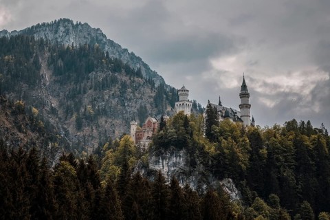 The impressive Neuschwanstein Castle on a dense, wooded hill under a dramatically cloudy sky,