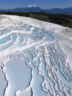 Cascading terraces of turquoise water and white limestone in the foreground, mountains in the