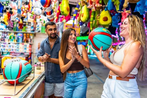 Happy friends enjoying a ball toss game at a lively amusement park, filled with colorful prizes and
