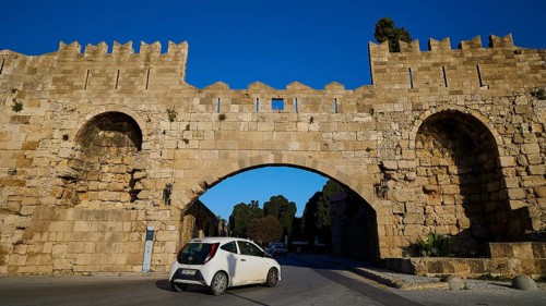 Arsenal Tor, Modern car drives through a historic stone gate on the road, harbour area, Rhodes