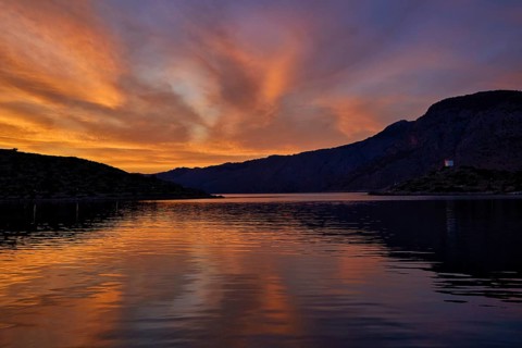 Colourful sunset over a calm lake with mountainous backdrop, Holy Week, Bay of Panormitis,