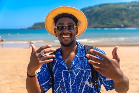 Young man wearing a hat and sunglasses, joyfully gesturing with his hands while enjoying the sunny