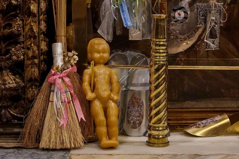 Symbolic objects in a religious context, including doll and broom, framed by gilded decorations,