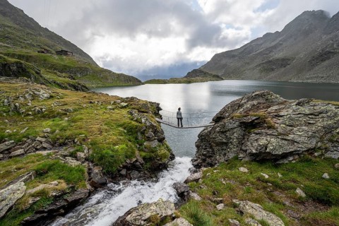 Mountaineer standing on a suspension bridge, mountain stream and mountain lake Wangenitzsee,