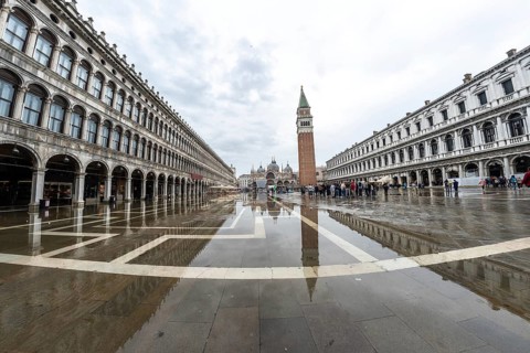 Tourists walking in flooded piazza san marco with campanile bell tower and saint mark's basilica on