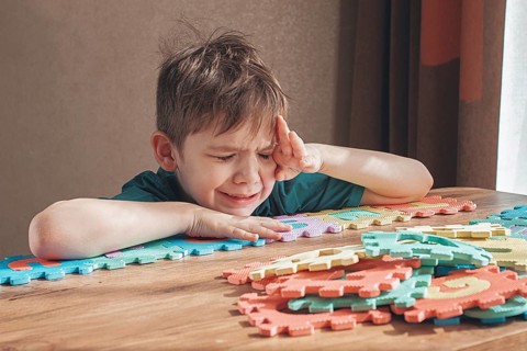 Boy with autism, expresses frustration, playing with puzzle pieces, on a wooden table, natural