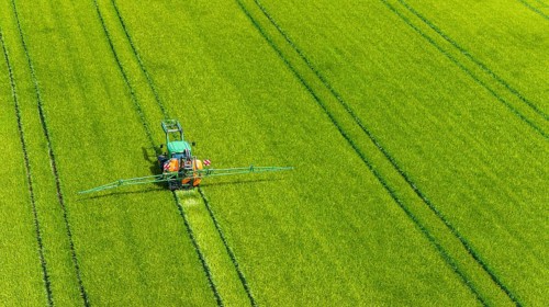 Farmer with tractor working in the field. In early summer, he fertilises the grain for an optimum
