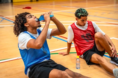 Two basketball players are sitting on the court, taking a break and drinking energy drinks after an