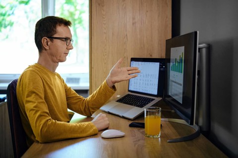 A middle-aged man in a yellow shirt gestures with his hand while presenting data on a monitor in a