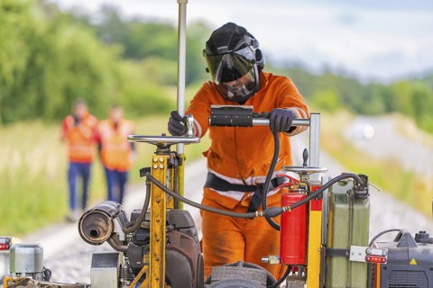 Welder on railway track, surrounded by machines, in the middle of a job, grinding work on the
