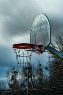 A solitary basketball hoop stands under overcast skies as dusk approaches. The chain net hangs