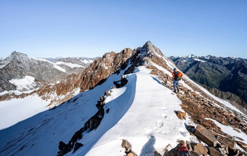 Mountaineer on rocky ridge with snow, mountain peak Wilder Freiger in the background, picturesque