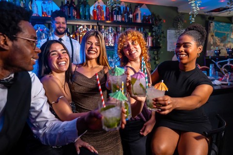 Cheerful group of friends raising glasses of mojito cocktails, enjoying nightlife at a vibrant bar