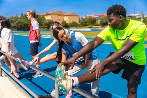 Track and field athletes stretching their legs on a railing by the track, preparing for a