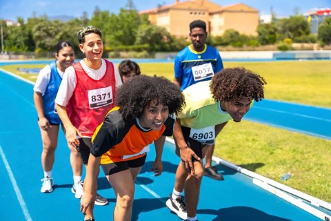 Diverse group of athletes crouching at starting line, preparing for a race on a blue running track