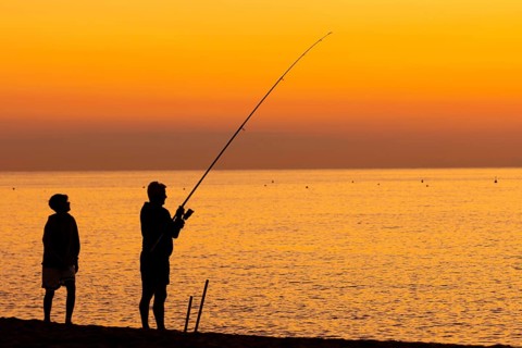 A man fishing just in front of sunrise on the Costa Rei, a coastline of the Italian island of