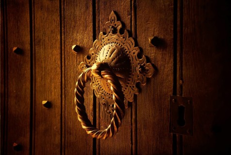 A beautifully designed door knocker sits prominently on a weathered wooden door. The warm lighting