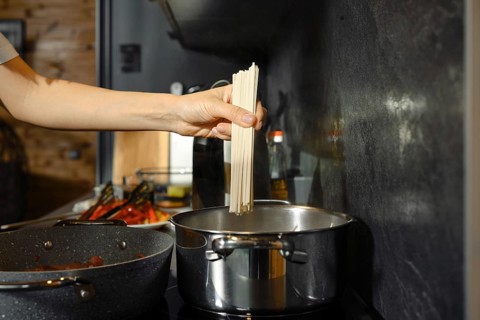 A person prepares a healthy pasta dish by adding uncooked noodles to boiling water in a