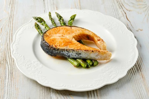 A gourmet dish features a beautifully grilled salmon steak served alongside fresh green asparagus
