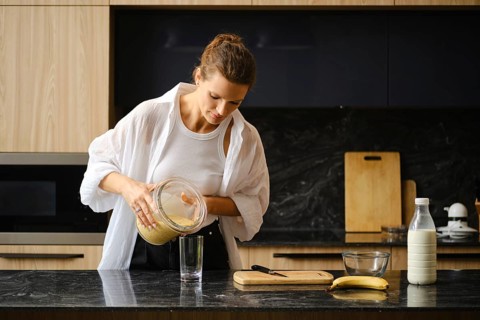 A person is preparing a healthy smoothie by pouring a blended mixture of banana and sea buckthorn