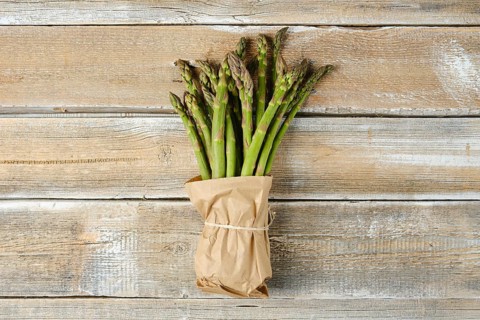 A bundle of fresh green asparagus is wrapped in brown paper and tied with twine, resting on a
