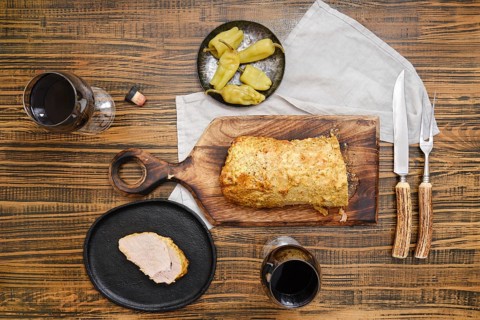 Overhead view of roasted pork meat and pickled peppers on a wooden table accompanied with red wine