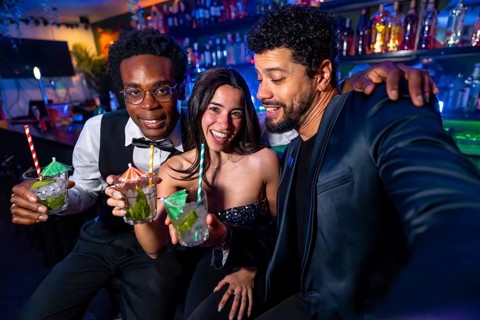 Happy friends taking a selfie while drinking cocktails at the bar, having fun together on a night