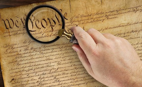 Male hand holding magnifying glass over the work people on the United States constitution