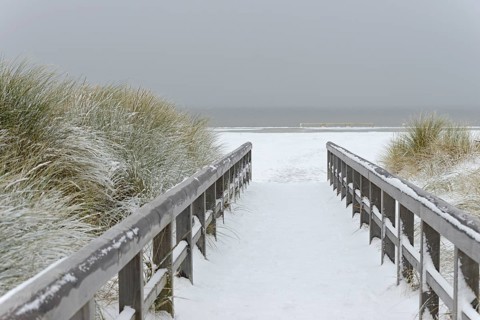 Winter day, onset of winter, wooden plank path leads through the snow-covered dune landscape to the