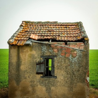 A small, abandoned structure shows signs of wear, with a crumbling roof and exposed brick. The