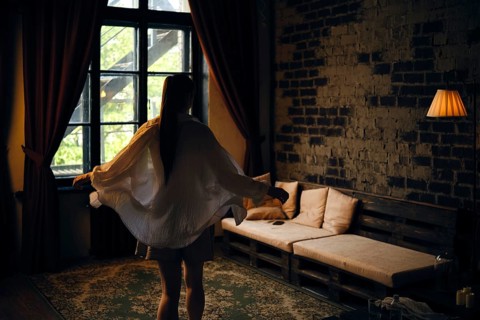 A woman in a light outfit twirls gracefully in a dimly lit room. Sunlight filters through large