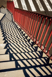 Bright sunlight creates intriguing patterns as shadows fall from red railings onto stone steps next