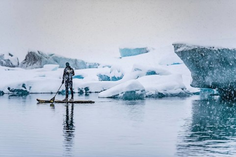 Man stand up paddling, snowfall, glacier lagoon Jökulsarlon at Vatnajökull, Iceland* Man stand up