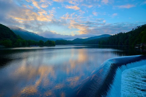 Calm lake with dam Paulushof-Absperrdamm, at dusk, surrounded by mountains and forests under a