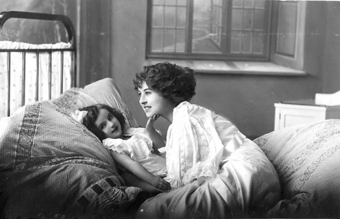 Woman with daughter, 1920s, A mother lies down with her child in bed, showing affection in a cosily