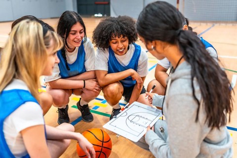 Basketball coach explaining game strategy to her young female athletes on a clipboard in a gym