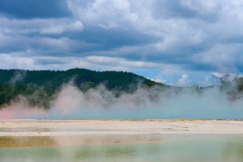 Misty steam over a hot spring and forested hills, under a dramatic sky, Champagne Pool thermal
