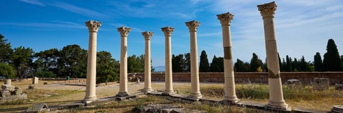 Row of ancient columns under blue sky, surrounded by vegetation, Temple of Apollo, Corinthian