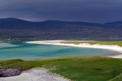 A tranquil beach with turquoise waters and dark, cloudy skies at the foot of mountains, Isle of