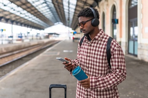 Stylish commuter using a mobile phone while enjoying music through headphones at a bustling train