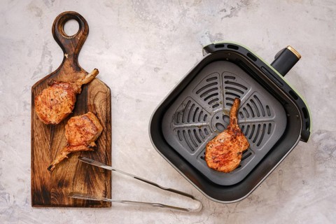 Juicy pork rib roast searing in an air fryer, alongside perfectly grilled chops resting on a wooden