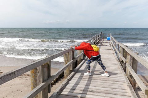 Woman in padded jacket doing stretching exercise with lunge on a wooden walkway on the beach,
