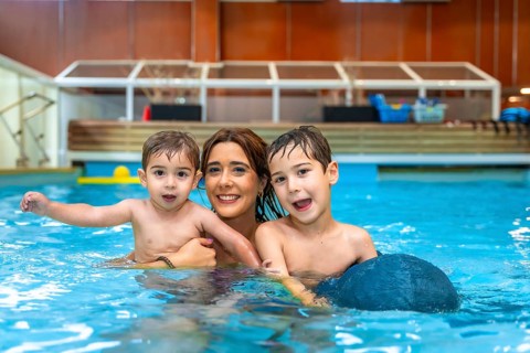 Mother and two sons smiling and playing in a swimming pool, enjoying a family moment of fun and