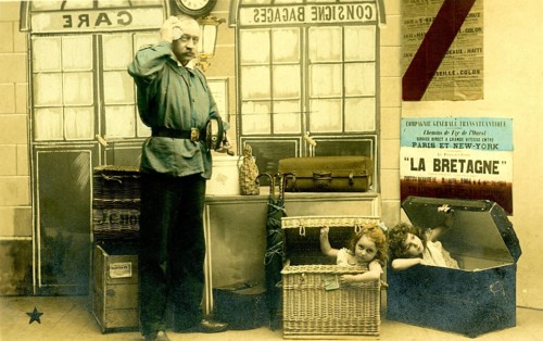 2 children in boxes, 1920, A man poses in a railway station environment while children humorously