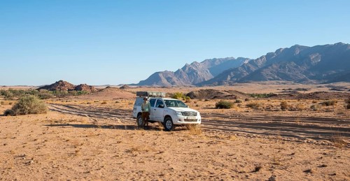 Tourist with off-road car on a sandy track, rock formation, Brandberg, Damaraland, Namibia