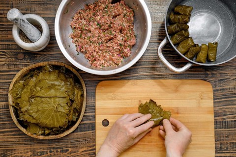 Grape leaves are being filled with a savory mixture of minced meat and rice at a home kitchen