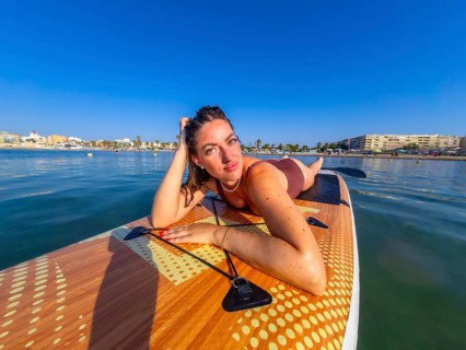 Young woman lying on a paddle board, soaking up the warm summer sun while enjoying the calm, serene