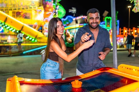 Young couple enjoying a game of air hockey at a brightly lit amusement park, adding excitement to